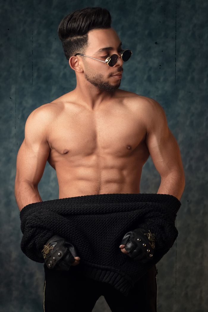Portrait of a shirtless muscular man wearing sunglasses in a studio setting.