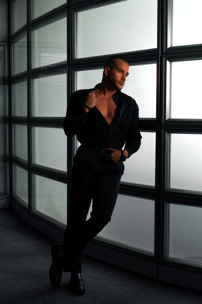 Sophisticated fashion photography featuring a man in a black outfit striking a pose indoors.