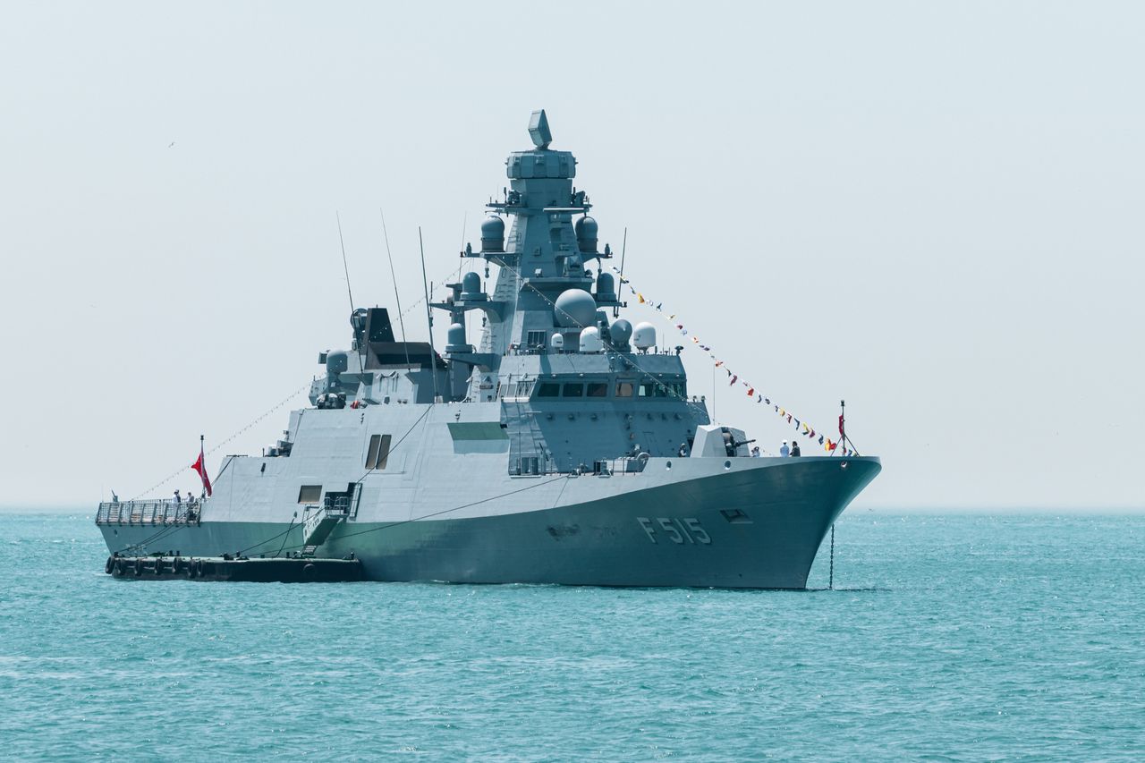 A naval warship with identification F515 sails on calm turquoise waters under a clear sky.