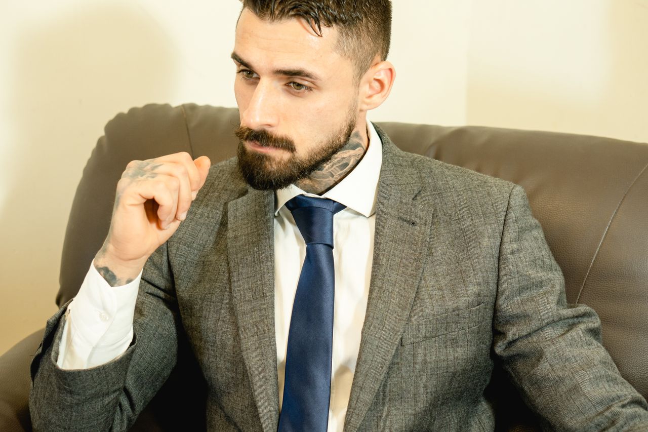 Portrait of a tattooed man in formal attire sitting on a leather chair.