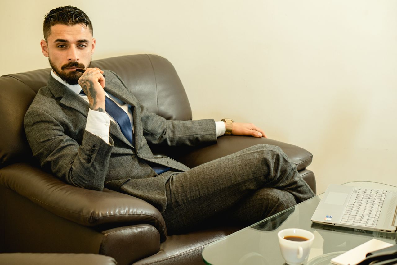 Pensive businessman in a suit sitting in an office chair with a laptop and coffee.